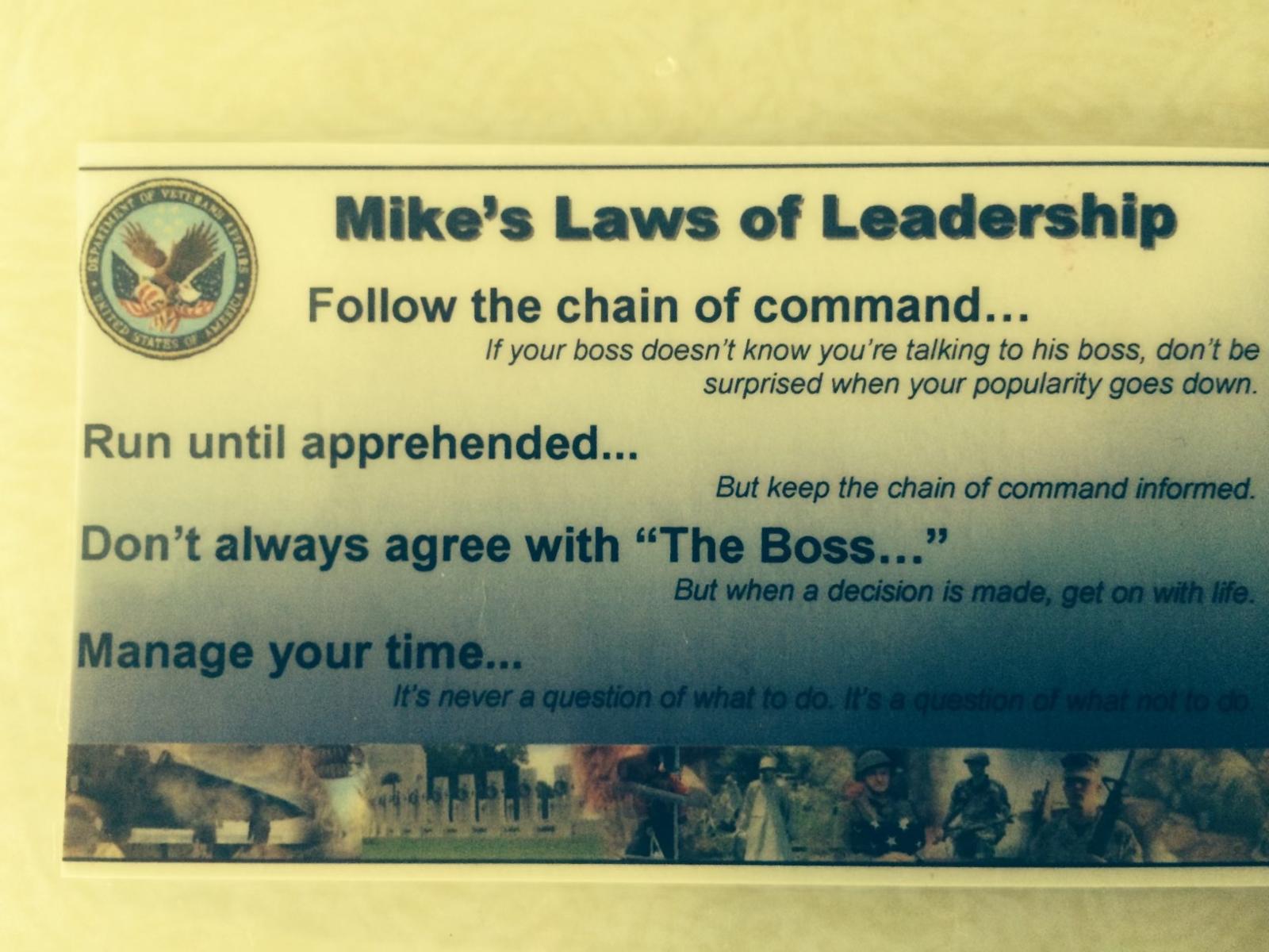 A laminated card titled "Mike's Laws of Leadership" listing four rules: Follow the chain of command... If your boss doesn't know you're talking to his boss, don't be surprised when your popularity goes down. Run until apprehended... But keep the chain of command informed. Don't always agree with "The Boss..." But when a decision is made, get on with life. Manage your time... It's never a question of what to do. It's a question of what not to do.